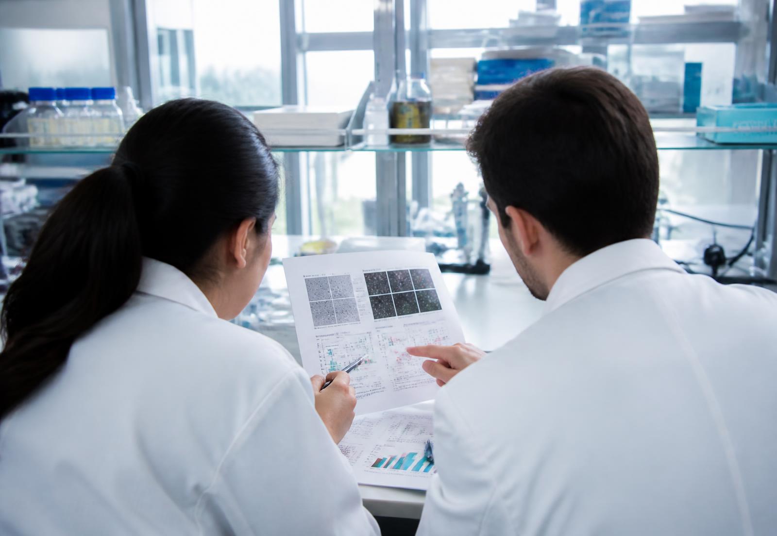 Two researchers reviewing printed assay figures together at a lab bench